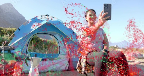 Smiling camper capturing smartphone selfie at mountain campsite with tent and moka pot, copy space