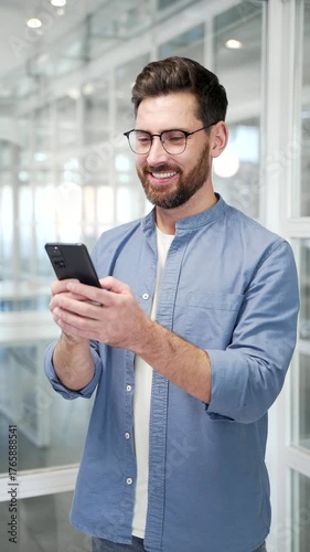 Businessman is using browsing mobile phone standing at workplace in a modern business office. Worker is chatting online, working in application or reading writing message on smartphone. Vertical video