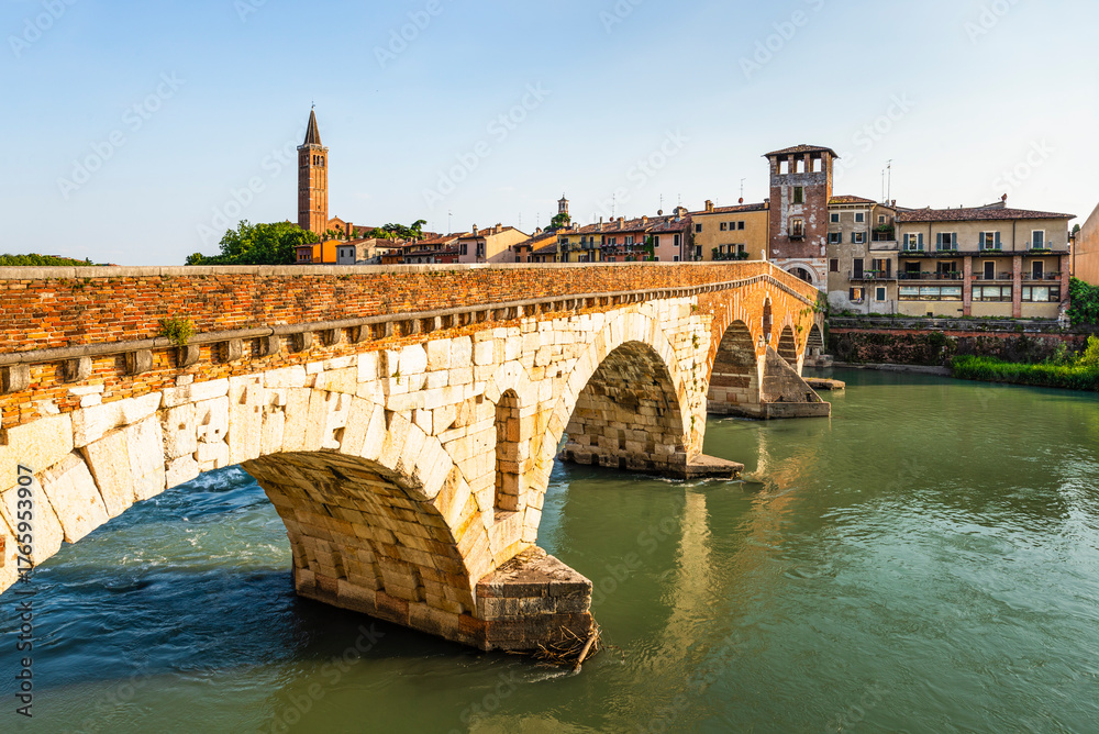 Fototapeta premium Die römische Ponte Pietra über dem Fluß Etsch in der Altstadt von Verona leuchtet in der Abendsonne, Venetien, Italien