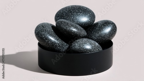 Black round bowl with six black stones inside. the stones are arranged in a pyramid-like formation, with the largest stone at the top and the smallest at the bottom.