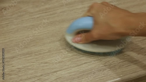 A person cleans a wooden surface using a round brush with a blue handle. The action reveals the surface's shine and removes dirt effectively. This cleaning method is simple and efficient.