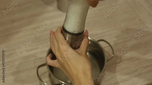 Hands are shown pouring salt from a grinder into a pot. The kitchen setting is simple and clean, highlighting the cooking process and essential techniques for meal preparation.