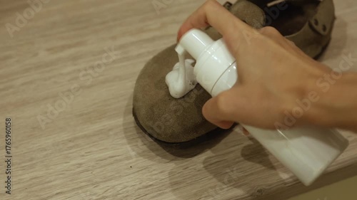 A person applies a foam solution to clean a shoe. The method shows careful application on the surface to maintain the shoe's quality. This routine ensures longer-lasting footwear.