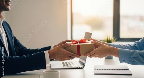 Business colleagues exchanging gift in office setting with laptop on desk