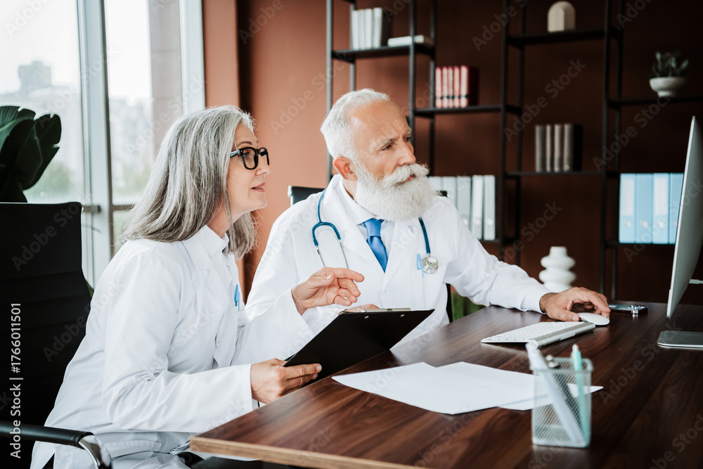 Fototapeta premium Two doctors in a bright clinic review patient files and discuss care while professionals collaborate in a modern hospital office
