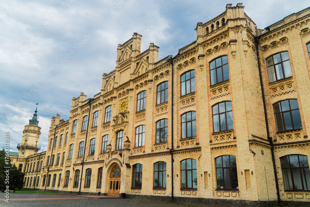 Fototapeta premium Low-angle view of the large yellow-brick facade of a historic university or technical institution building with decorative masonry and a prominent corner tower