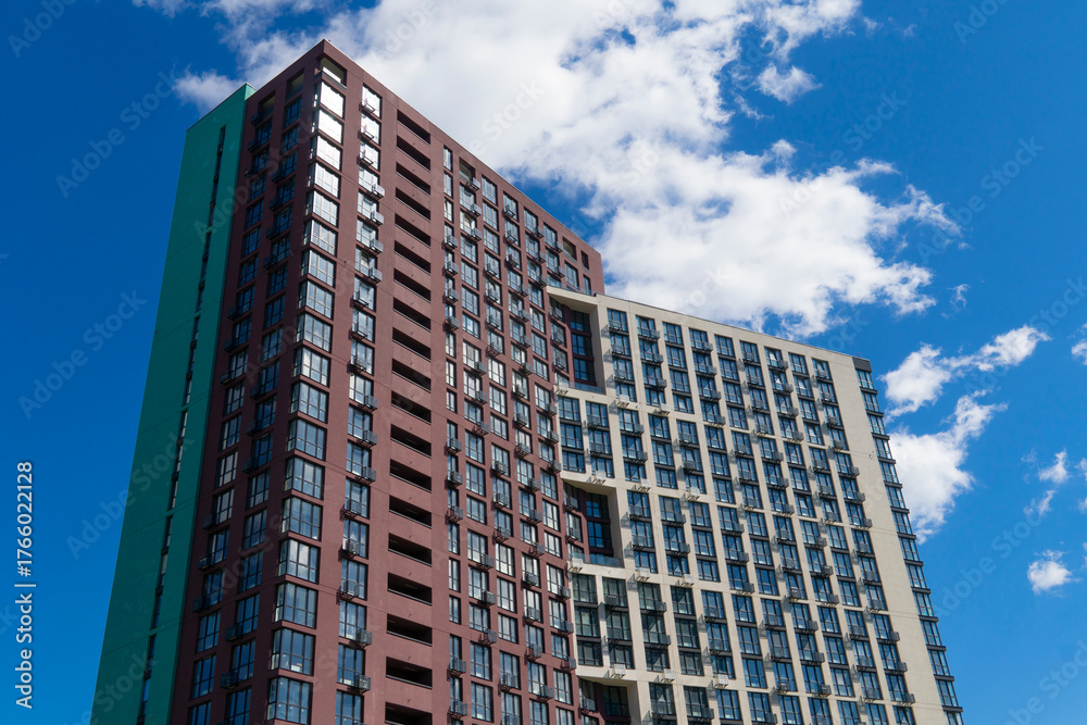 Naklejka premium Striking architectural detail of a contemporary high-rise apartment building with contrasting colored facades set against a dramatic, cloudy blue sky