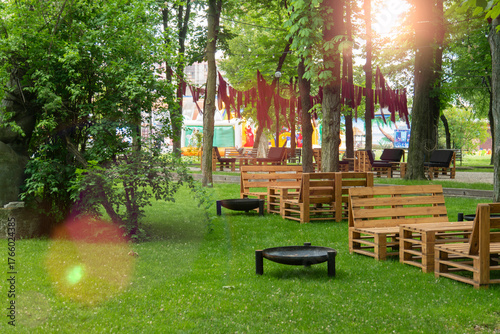 Cozy outdoor lounge and dining area in a green park with handmade rustic wooden pallet furniture and fire pits under the canopy of trees