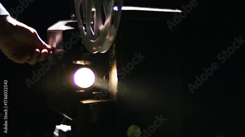 Bright light beam from a vintage film projector turning on in a dark room, with the film reel spinning and projecting light with a cinematic lens flare, representing nostalgia and cinema