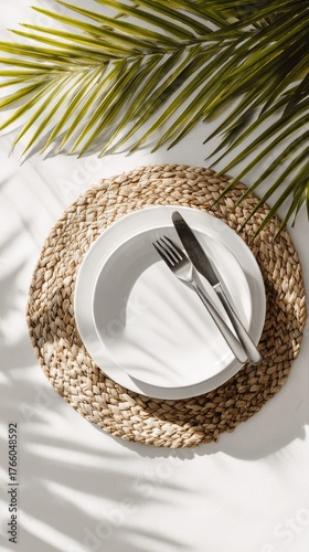 Elegant Dining Setup With White Plate and Cutlery Surrounded by Green Palm Le...