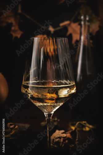 Close-up of white wine glass with golden reflections and soft autumn tones in moody background