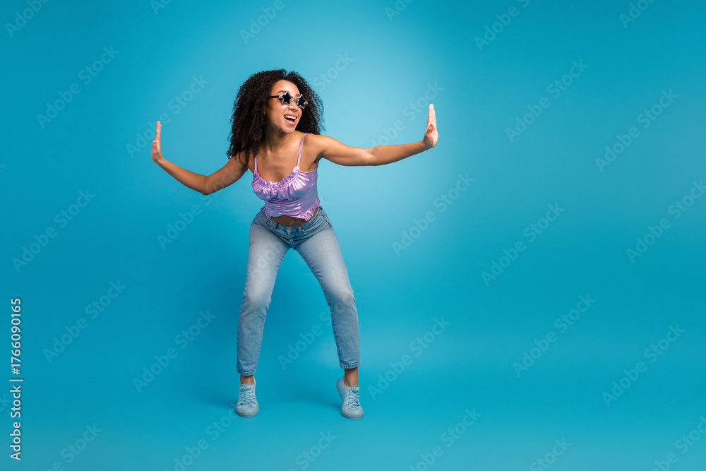 Obraz premium Young woman in purple top and jeans dances with open arms against blue background conveying energy confidence