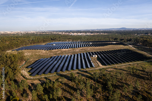 Aerial drone view of rows of solar panels in lush fields under sky generating sustainable energy with scenic townscape in background 