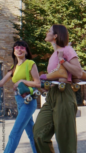 Women stroll along quiet street with quad skates on shoulders