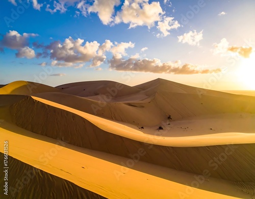 Fototapeta Naklejka Na Ścianę i Meble -  Aerial view of sand dunes under a blue sky with fluffy clouds and warm sunlight