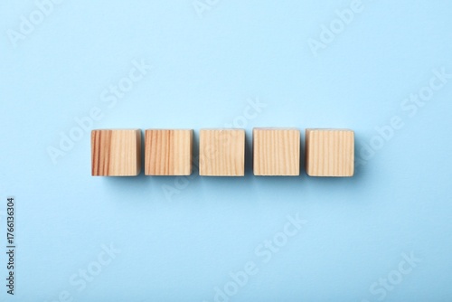 Wooden cubes on light blue background, top view
