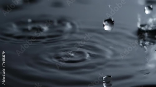 Extreme close-up slow motion shot of crystal clear rain droplets falling and splashing onto a dark, reflective surface wet, extreme, splash