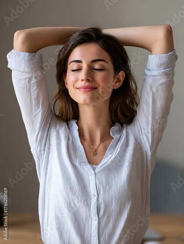 A calm Eastern woman pausing at her desk, taking a mindful moment to practice deep breathing during a busy workday