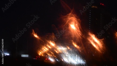 Water drops on the windshield of a car, inside the car when it rains on a city street. Blurred background, red and orange bokeh, Blurred lights outside window when it rains at night