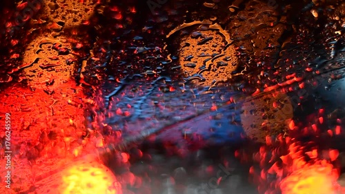 Water drops on the windshield of a car, inside the car when it rains on a city street. Blurred background, red and orange bokeh, Blurred lights outside window when it rains at night