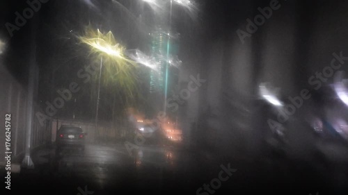 Water drops on the windshield of a car, inside the car when it rains on a city street. Blurred background, red and orange bokeh, Blurred lights outside window when it rains at night