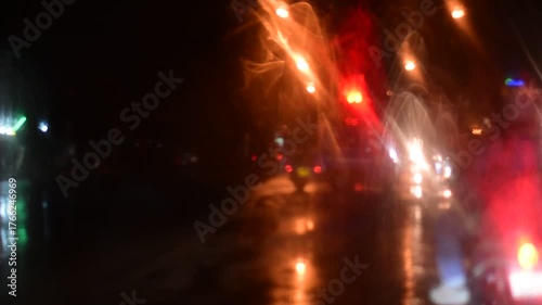 Water drops on the windshield of a car, inside the car when it rains on a city street. Blurred background, red and orange bokeh, Blurred lights outside window when it rains at night