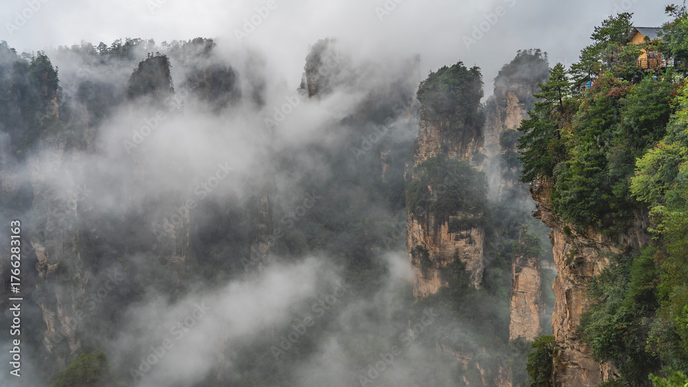 Fototapeta premium Mystical mountain landscape. The high cliffs pillars are shrouded in fog. Peaks in the clouds. Green vegetation on steep slopes. China. Zhangjiajie National Forest Park. Avatar