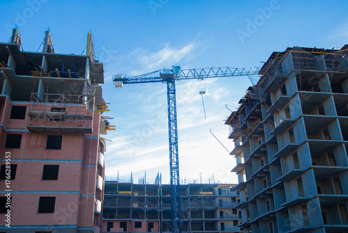 The construction of two large buildings, surrounded by cranes and scaffolding, against a clear blue sky, demonstrates the development of the city and architectural progress. The concept of
