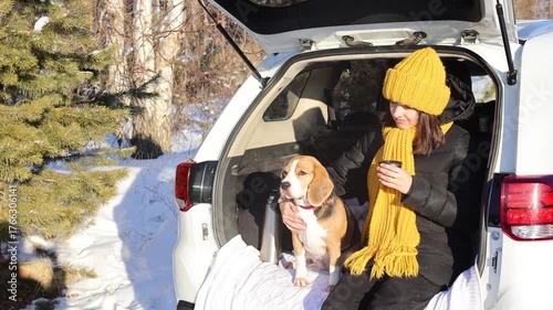 Happy girl  is sitting in the trunk of a car with her beagle dog . Winter travel by car with a pet.