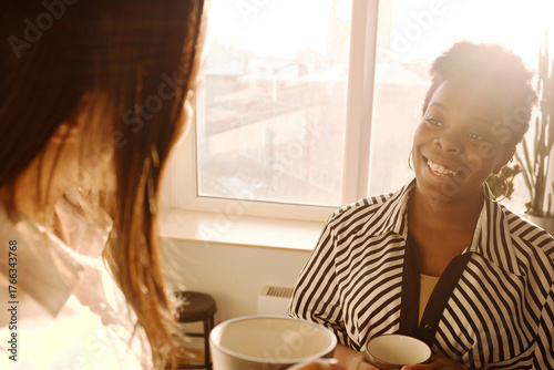 Obraz na plátně Attractive black woman listening to female colleague and smiling cheerfully whil