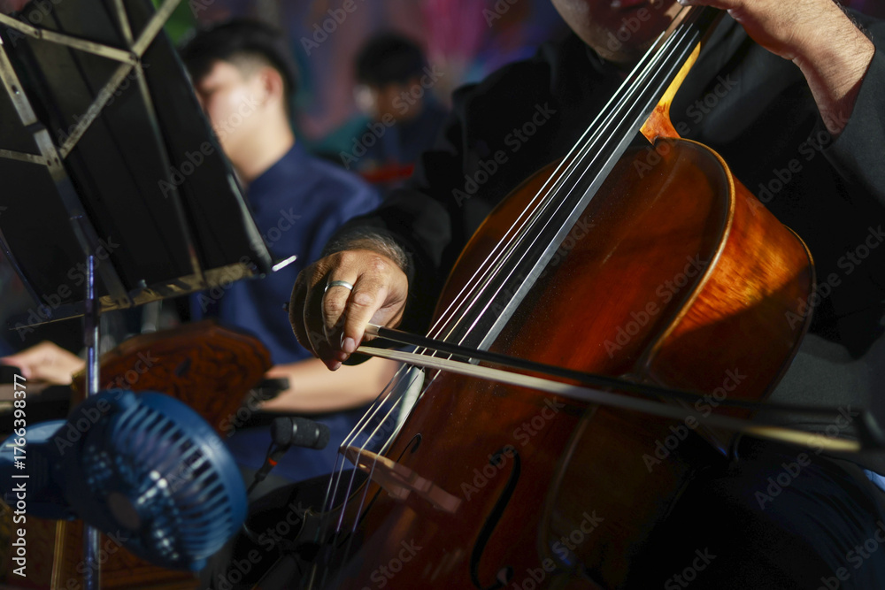 Fototapeta premium Focused musician playing cello in classical music orchestra concert. This passionate performance shows close up of hand, bow, and string instrument during symphony