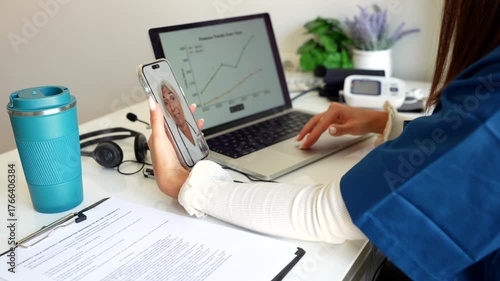 Medical professional engaging in a remote consultation with a patient via smartphone, using a laptop to review health data and waving goodbye at the end of the online medical appointment
