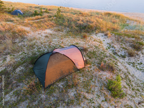 Fototapeta Naklejka Na Ścianę i Meble -  Aerial drone view of wild camping tents on sandy dunes by the Baltic Sea beach in Estonia. Beautiful nature landscape at sunset.