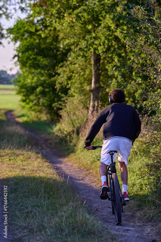 Cyclist riding bike on rural dirt path through green countryside meadow summer outdoor recreation Germany vertical
