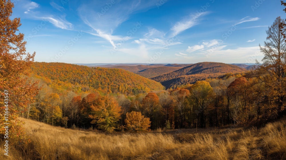 Fototapeta premium A scenic view of rolling hills covered in autumn foliage under a partly cloudy blue sky landscape scene