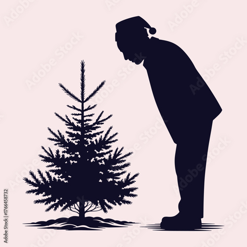 Silhouette of a man wearing a Santa hat looking down at a small Christmas tree pine tree