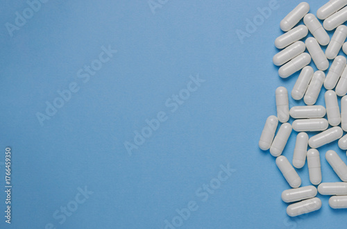 White medical capsules scattered on a blue background with space for text. Concept of medicine and patient treatment.
