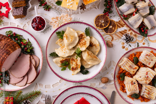 Classic Christmas food medley on a decorated table. Fish, dumplings stuffed with cabbage and mushrooms, cheesecake, and ham.