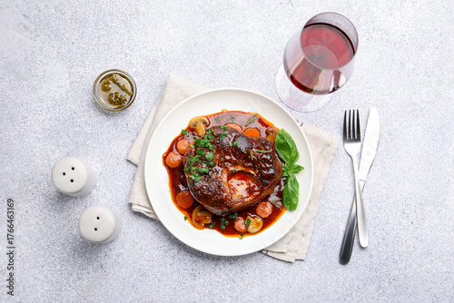Foto Tasty beef ossobuco with carrot, mushrooms and herbs served on grey textured tab
