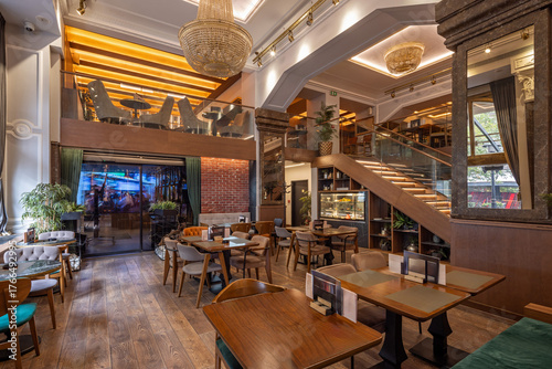 Stylish double-level restaurant featuring wooden décor, chandeliers, and warm ambient lighting