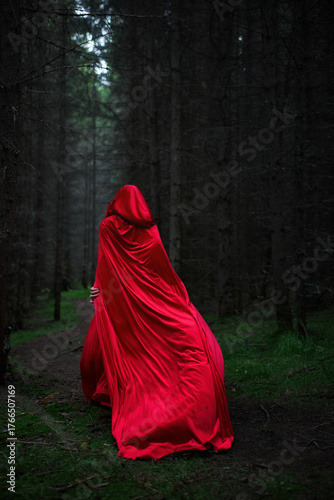 figure clad in a flowing red cloak wanders through a dark forest. Tall trees surround the path, creating an eerie yet captivating atmosphere as twilight descends