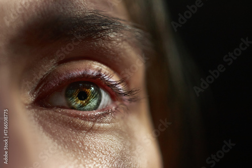 close-up view of a human eye showcases a blend of green and gold hues. light reflects off the eyelashes, creating a serene and thoughtful mood in the cozy indoor atmosphere