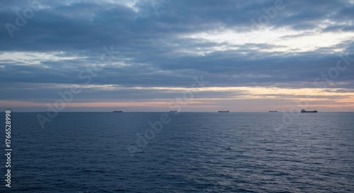 Calm ocean horizon with ships near dusk, under a partly cloudy, soft-lit, tranquil sky
