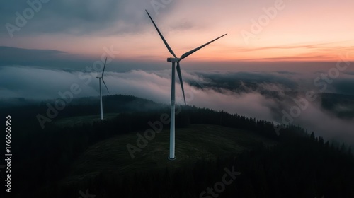 Wind turbines silhouetted against a dreamy sunset sky with atmospheric fog rolling through the hills