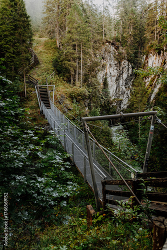 Metal suspension bridge in the Alps near Namlos, Tyrol – hiking trail through dense mountain forest across a deep gorge