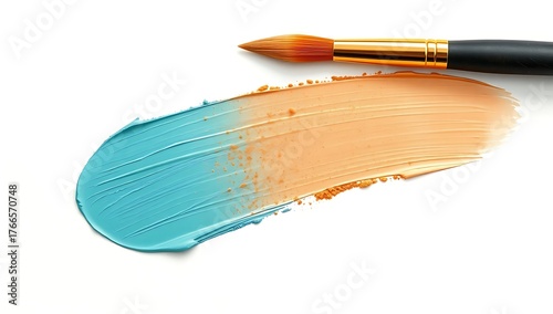 A paintbrush lying on a stroke of blue and orange paint on a white surface in a studio setting