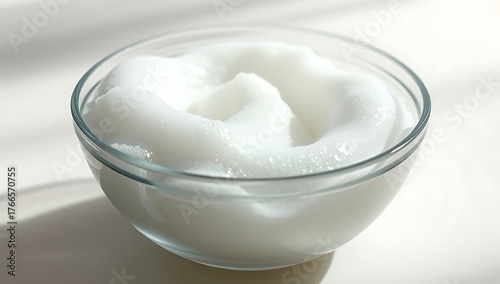 A clear glass bowl filled with a thick white substance sitting on a white surface in bright light