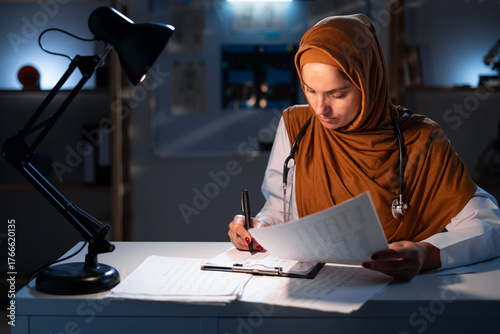 Muslim doctor woman with clipboard in office working on night shift in hospital with healthcare, reading paperwork, application and health insurance
