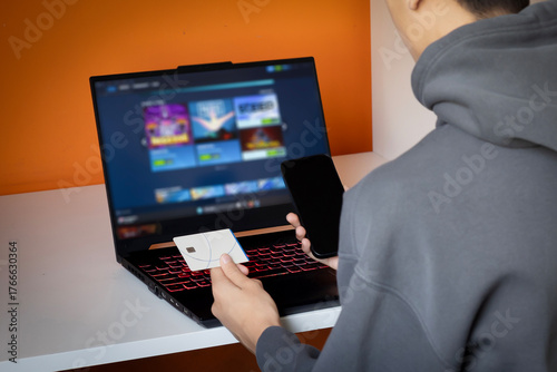 Teenager boy holding credit card with mobile phone purchasing virtual items using stolen credit card information. Capture for Credit Card Fraud Among Teen Gamers.