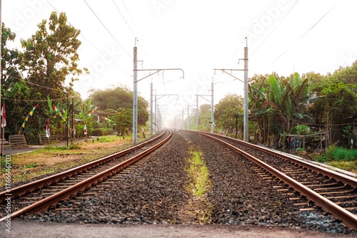 A straight-on, low-angle view of two parallel train tracks extending into the distance through a rural area on a sunny day.